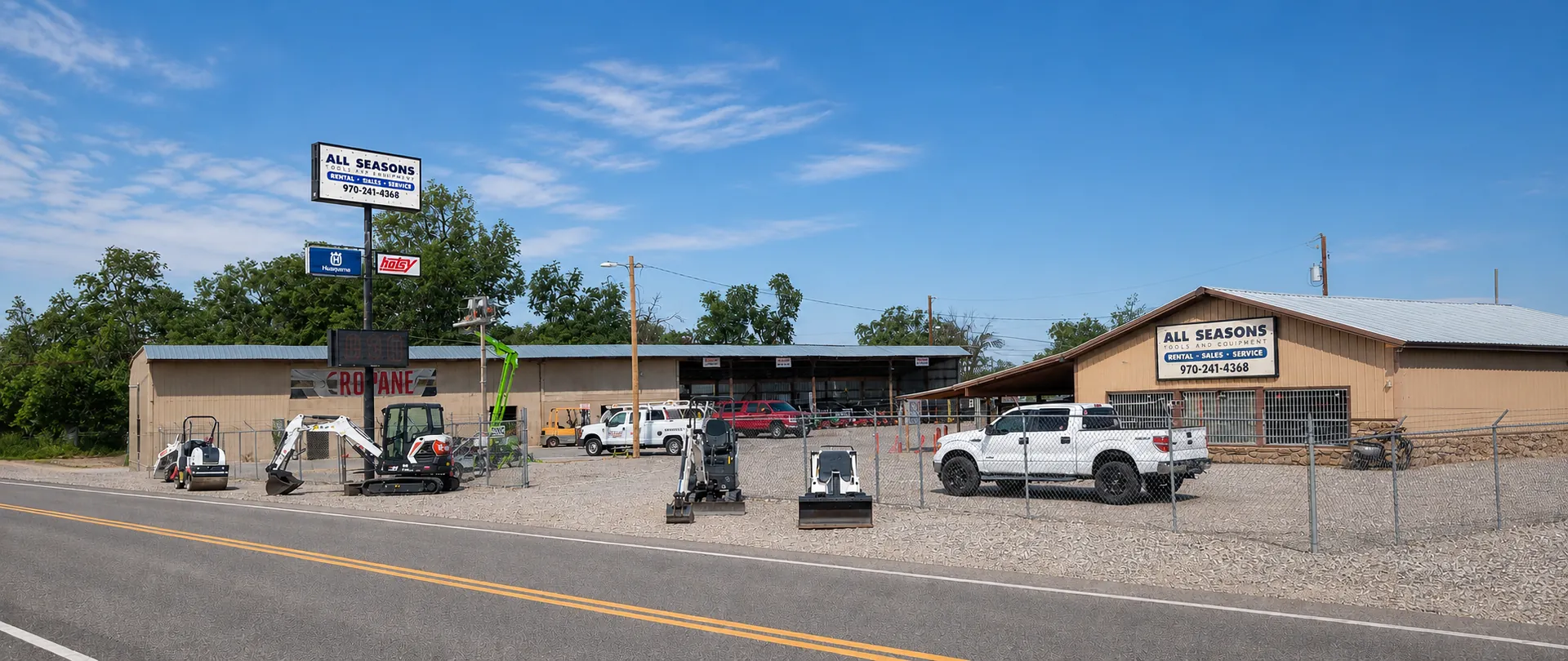 All Seasons Rentals storefront in Grand Junction, Colorado on a clear day, with excavators, a roller and service trucks in the yard